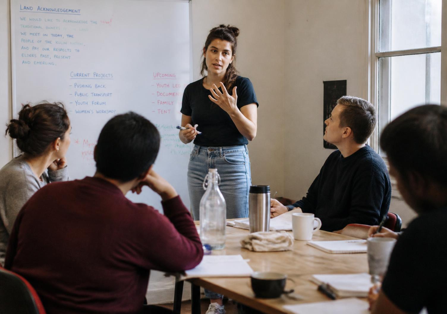A young professional presenting to a small seated team in a daylight room